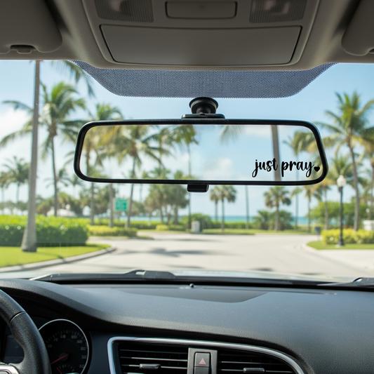Car interior with a rearview mirror displaying 'just pray' text, palm trees in the background.